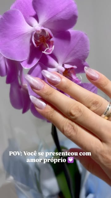 Unhas rosadas de efeito perolado ao lado de uma orquídea
